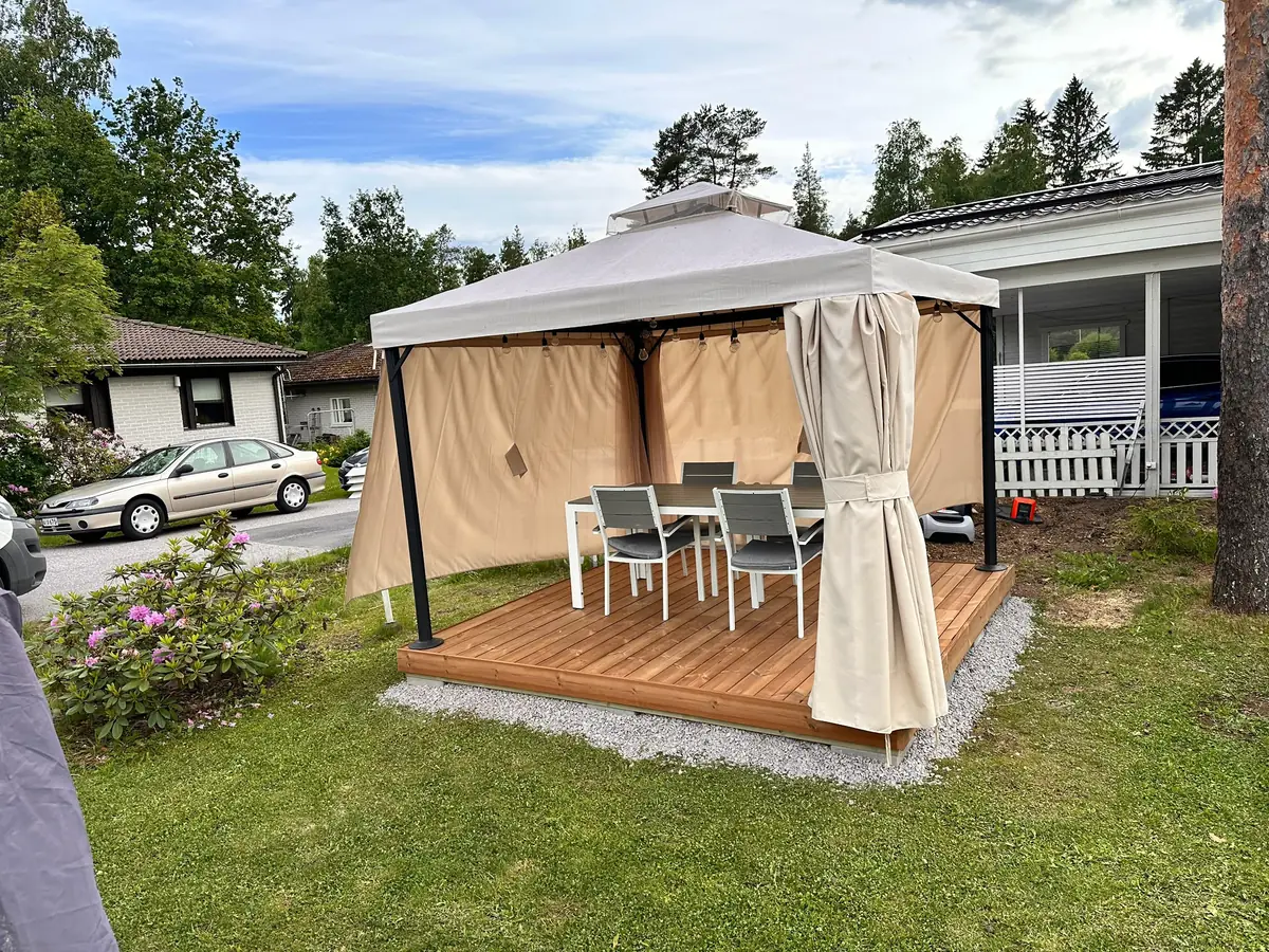 NextBuildin rakentama terassi, jolla paviljonki, pöytä ja tuolit kesäisessä pihassa